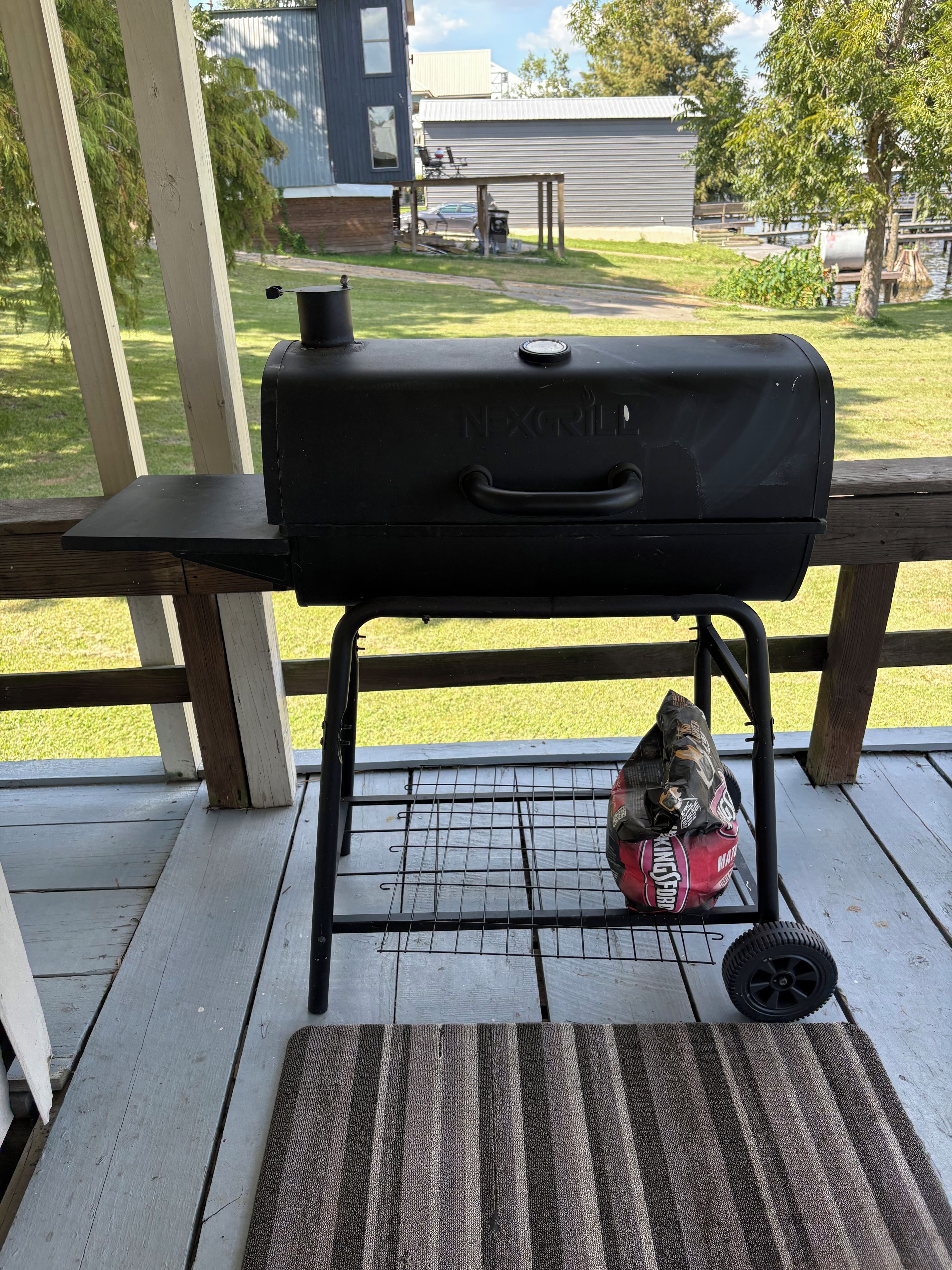 A barbecue grill on a wooden deck with a bag of charcoal underneath.