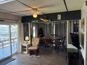 A room with a dining table, chairs, a television, and a view of a dock and water outside.