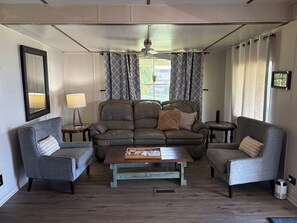 A living room with a sofa, two armchairs, a coffee table, a lamp, and a ceiling fan.