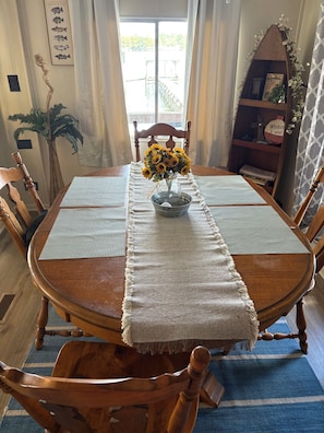 A wooden dining table with a vase of sunflowers, surrounded by chairs, a placemat, and a decorative wall with a fish chart.