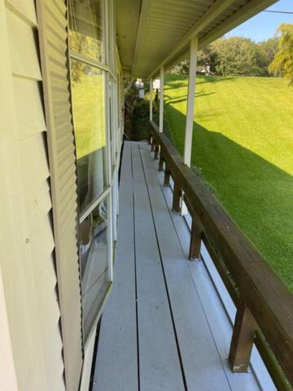 A covered porch with a wooden railing, a grassy yard, and a house in the background.