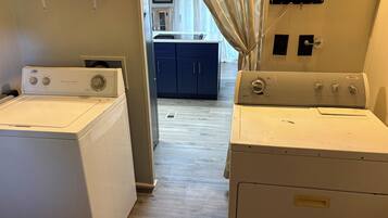 A laundry room with two front-loading washers and dryers, a wooden floor, and a view into the kitchen area.