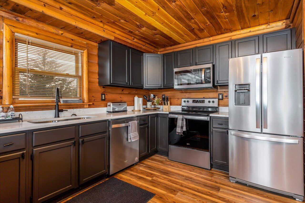 A modern kitchen with dark cabinets, stainless steel appliances, and a wooden ceiling.