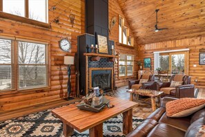 A log cabin interior with a fireplace, leather furniture, and large windows. - Amazing Log Cabin with Beautiful Views at Apple Canyon Lake (Apple River)