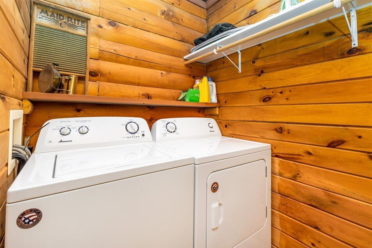 Un espace buanderie compact comprenant un lave-linge et un sèche-linge Amana à chargement frontal, des murs en bois et une étagère contenant des produits de nettoyage.