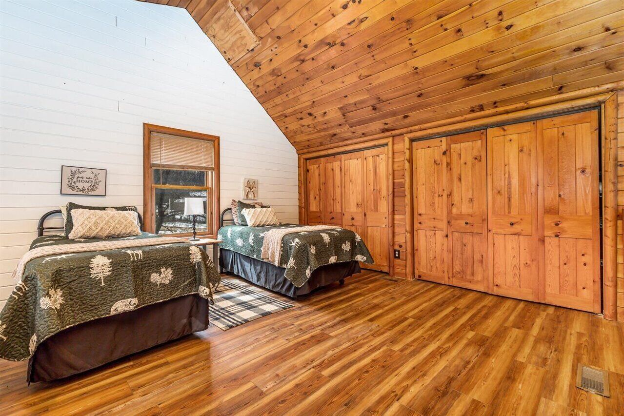A cozy bedroom with two beds, wooden walls, and a sloped ceiling.