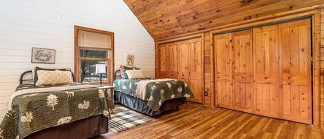A cozy bedroom with two beds, wooden walls, and a sloped ceiling.