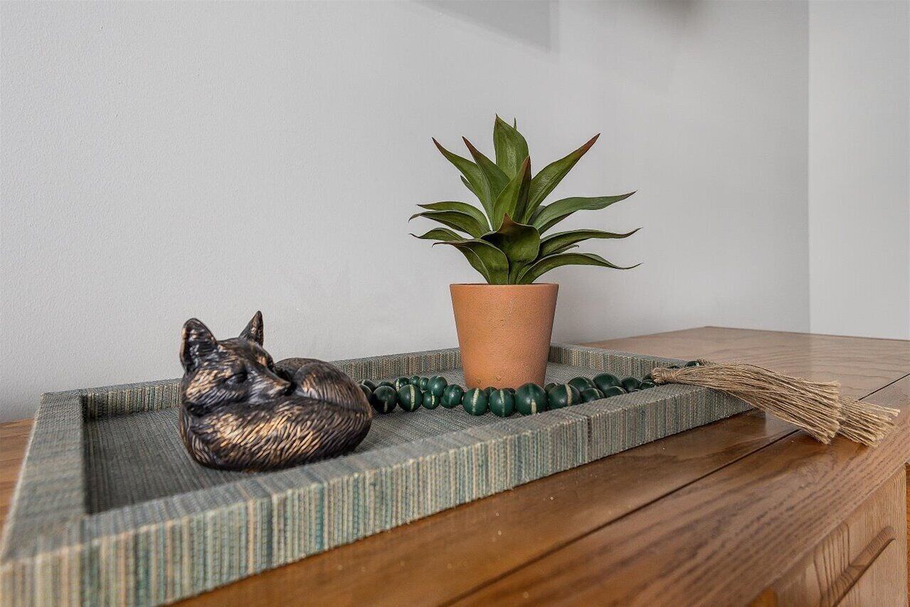 A wooden table with a terracotta pot containing a green plant, a ceramic dog figurine, and a woven mat.
