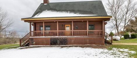 Une cabane en rondins avec un porche, une cheminée et un paysage enneigé.