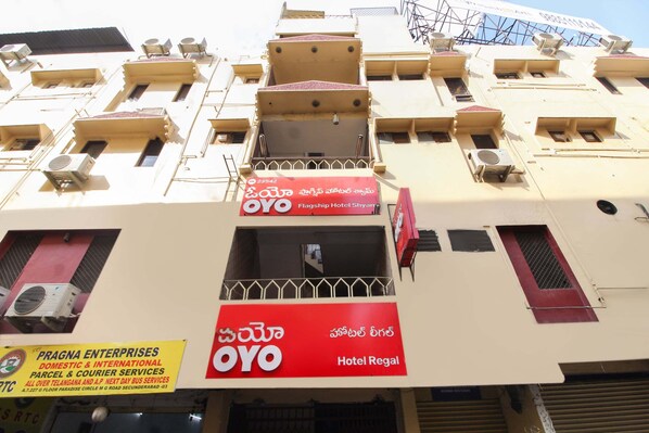 A hotel with multiple balconies, a prominent red sign for OYO Hotel Regal, and a sign for Pragna Enterprises offering parcel and courier services.