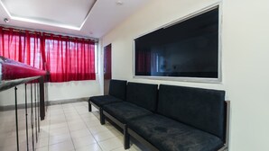 A room with a black sofa, a red curtain, a white ceiling fan, and a large window. - OYO 70733 Hotel Regal (Hyderabad)