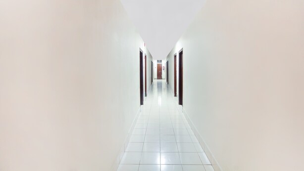 A long, narrow hallway with white walls and a tiled floor, leading to a door at the end. - OYO 70733 Hotel Regal (Hyderabad)