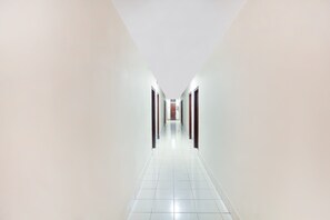 A long, narrow hallway with white walls and a tiled floor, leading to a door at the end.