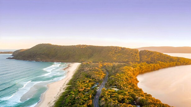 A coastal landscape with a beach, a road, and a forested hill. - Tiona Palms Holiday Park (Tiona)