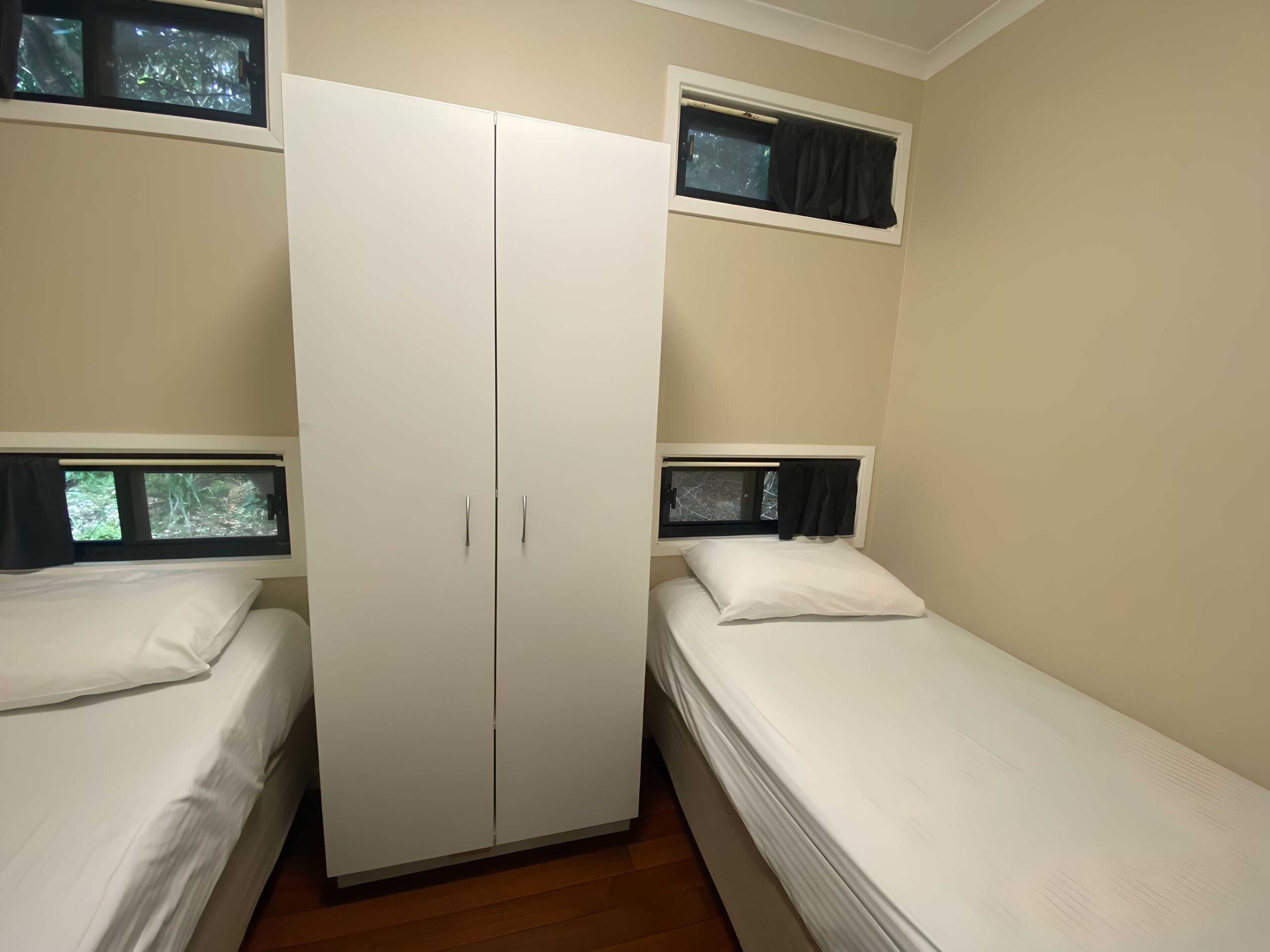 A room with two single beds, a wardrobe, and windows with curtains.