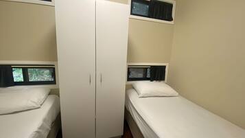 A room with two single beds, a wardrobe, and windows with curtains.