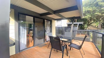 A balcony with a wooden deck, a glass door leading to a patio, and a table with chairs.