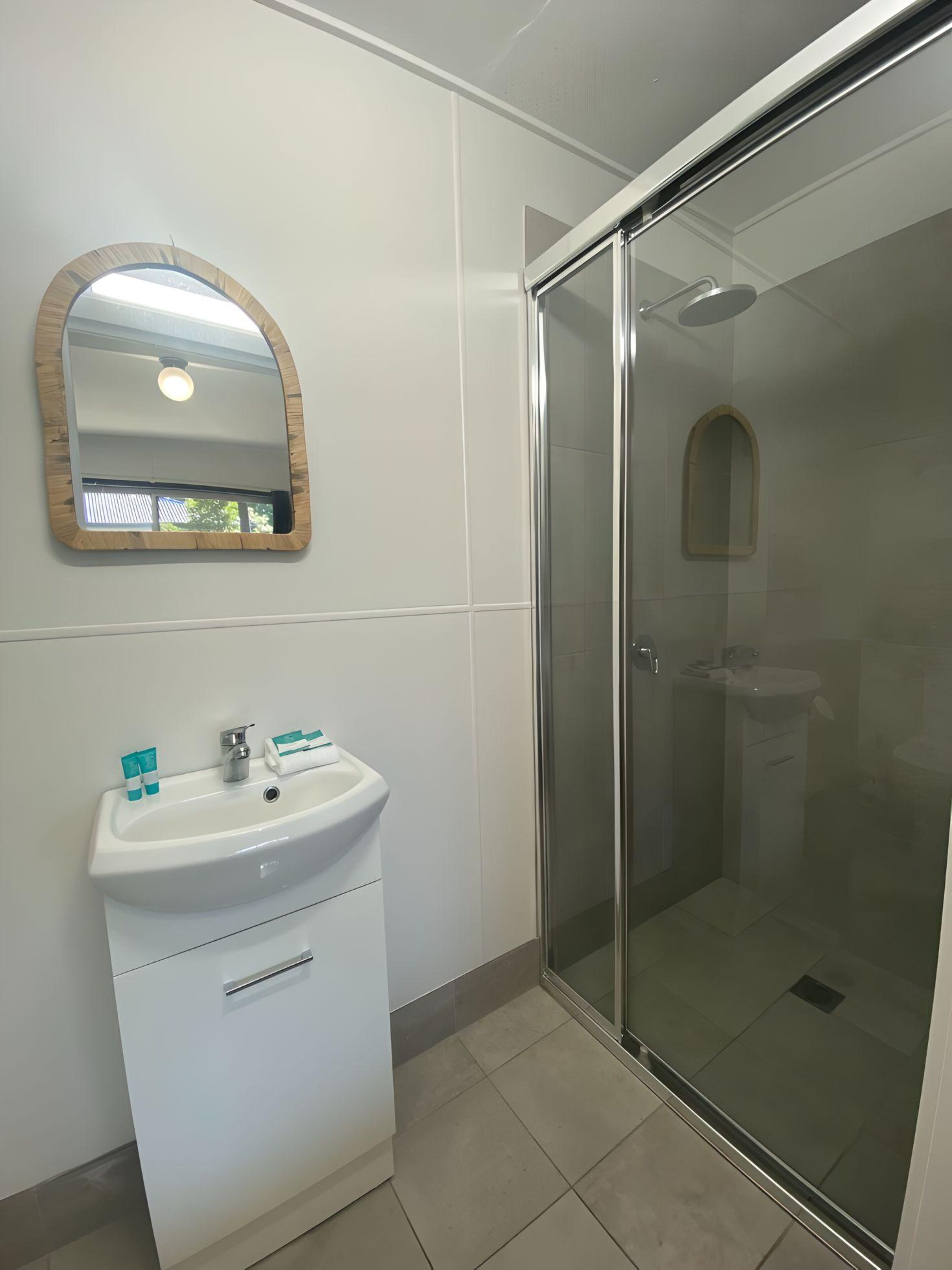 A bathroom with a white sink, mirror, and glass shower enclosure.
