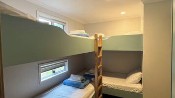 A compact room with bunk beds, a window with blinds, and a built-in shelf.