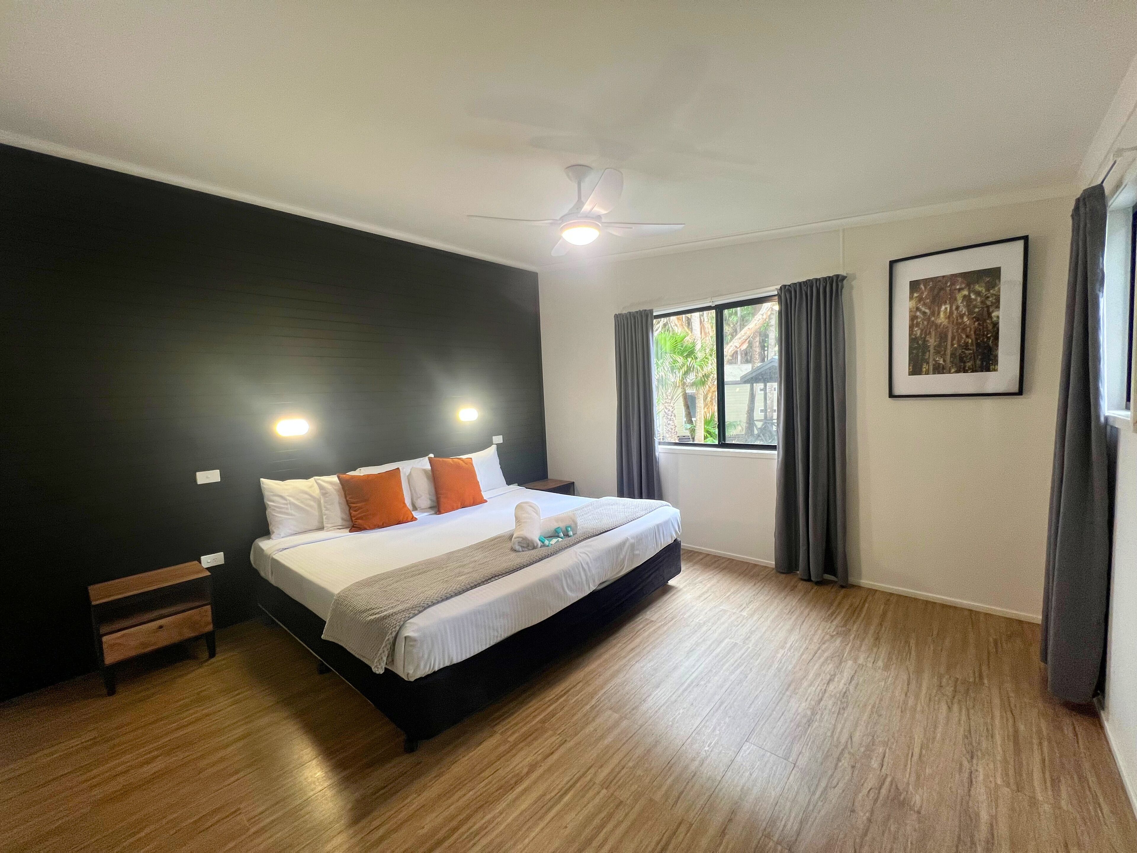 A bedroom with a bed, a ceiling fan, a window with curtains, and a framed picture on the wall.