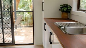 A modern kitchen with a wooden countertop, a stainless steel sink, and a sliding glass door leading to an outdoor patio. - Tiona Palms Holiday Park (Tiona)