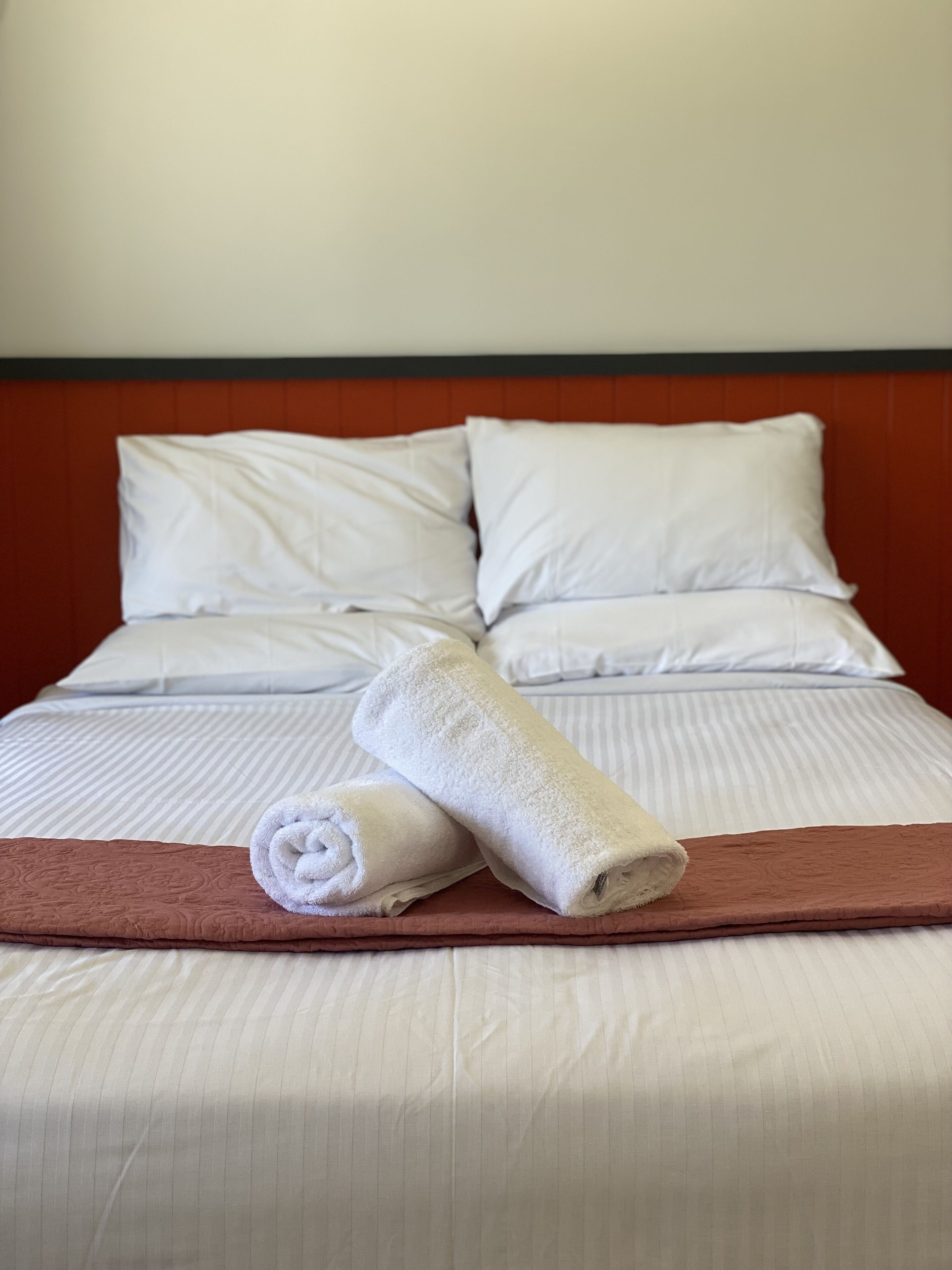 A neatly made bed with white linens, a brown throw blanket, and two rolled towels.