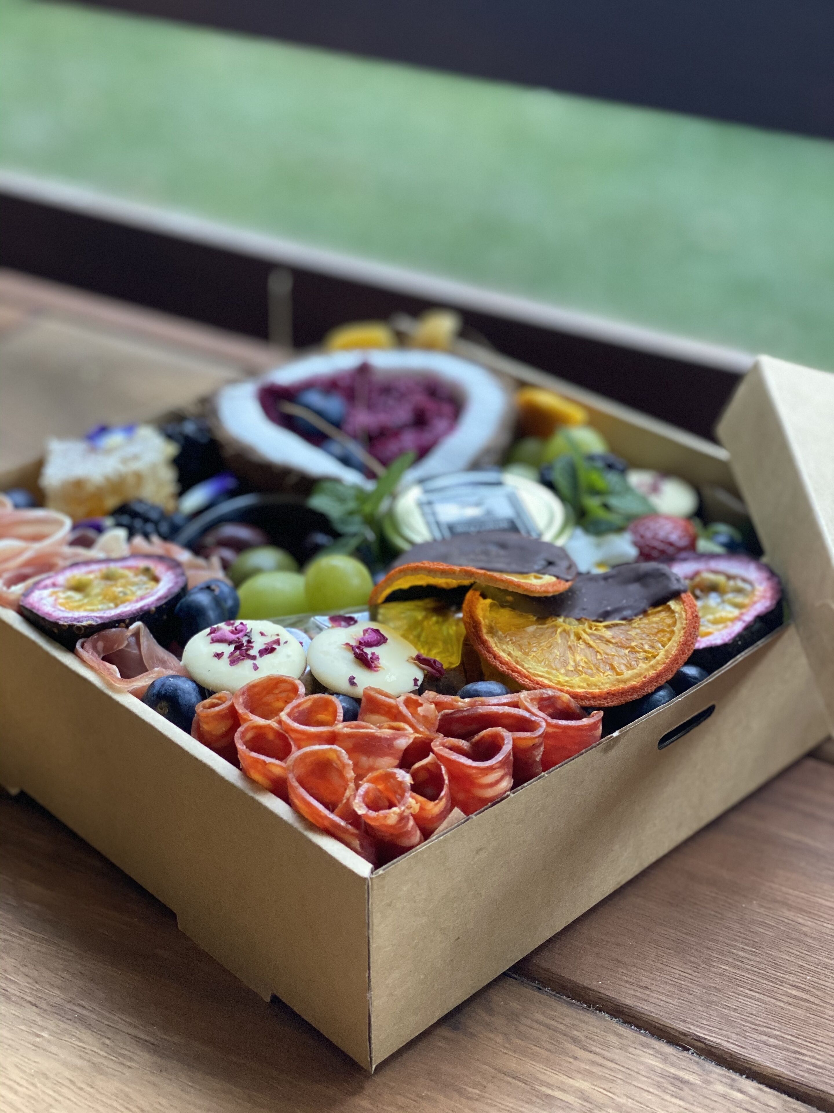 Une boîte contenant un assortiment de collations, notamment des fruits, des noix et du fromage, posée sur une table en bois.