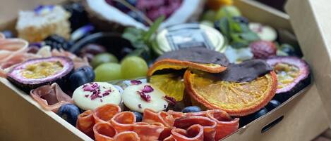 Une boîte contenant un assortiment de collations, notamment des fruits, des noix et du fromage, posée sur une table en bois.