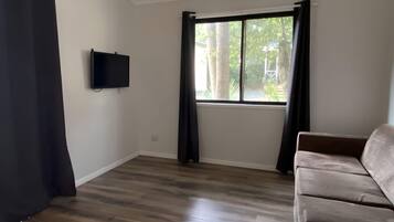A room with a large window, a flat-screen TV mounted on the wall, and a brown sofa.