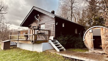 Escape to a secluded cabin with a gabled roof and wooden deck, surrounded by trees and a grassy area.