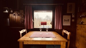 Una mesa de madera con dos sillas, una ventana con cortinas y vista a un banco rojo en el exterior.