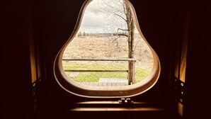 Una ventana con un marco original en forma de pera, que da a un campo de césped y árboles.