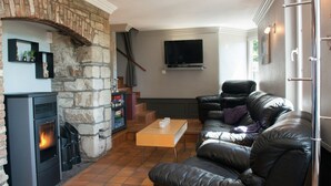 A cozy living room with a stone fireplace, leather sofa, and a flat-screen TV mounted on the wall. - Alluring Holiday Home in Malmedy With Sauna (Malmedy)