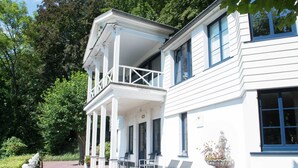 A two-story white building with a balcony and a covered porch. - Alluring Holiday Home in Malmedy With Sauna (Malmedy)