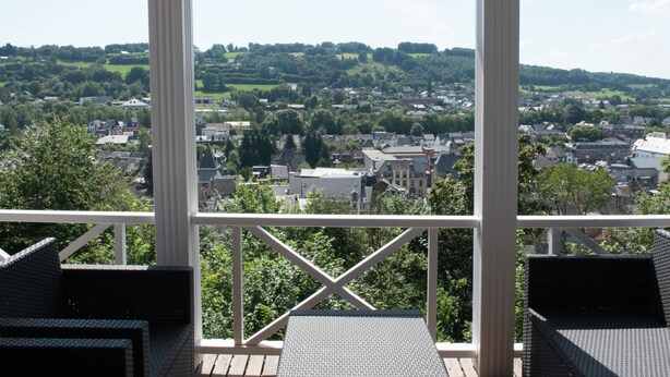 A covered outdoor seating area with a view of a town and surrounding greenery. - Alluring Holiday Home in Malmedy With Sauna (Malmedy)