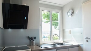 A compact kitchen with a built-in oven, a dishwasher, and a microwave. There's a window with a view of greenery outside, and a clock on the wall. - Alluring Holiday Home in Malmedy With Sauna (Malmedy)