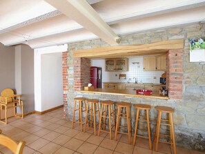 Una cocina con pared de piedra, taburetes de madera y un refrigerador.
