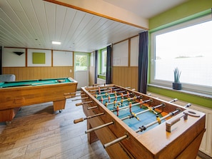 Une table de billard et une table de baby-foot dans une pièce au plancher de bois, avec une fenêtre offrant une vue et un mur vert.