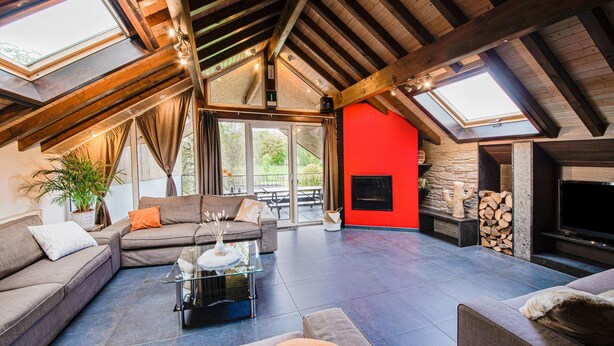 A spacious loft with a high ceiling, a fireplace, a sofa, and a TV. - Charming Cottage with Hot Tub & Sauna, High Fens (Waimes)