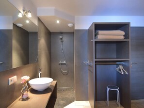 Bathroom features a large mirror, vessel sink, shower with handheld showerhead, and shelf.