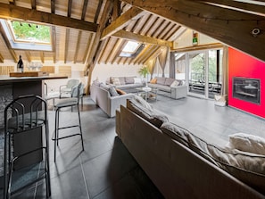 An attic-style room with a high ceiling, exposed wooden beams, a large window, and a red accent wall.