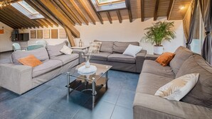 A loft-style living room with exposed wooden beams, a sectional sofa, a glass coffee table, and a potted plant. - Charming Cottage with Hot Tub & Sauna, High Fens (Waimes)