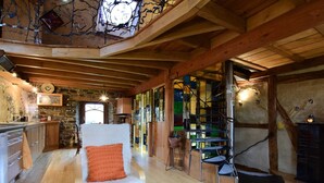 A rustic interior with a wooden staircase, a white armchair, and a kitchen area. - Holiday Home in Longueville Near Forest (Durbuy)