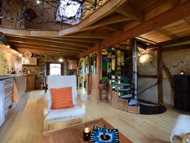 Un interior rústico con una escalera de madera, un sillón blanco y una zona de cocina.