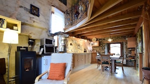 A rustic kitchen with wooden beams, a stone wall, and a dining area with a wooden table and chairs. - Holiday Home in Longueville Near Forest (Durbuy)