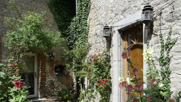 A stone building with a wooden door, a brick pathway, and various plants and flowers. - Holiday Home in Longueville Near Forest (Durbuy)