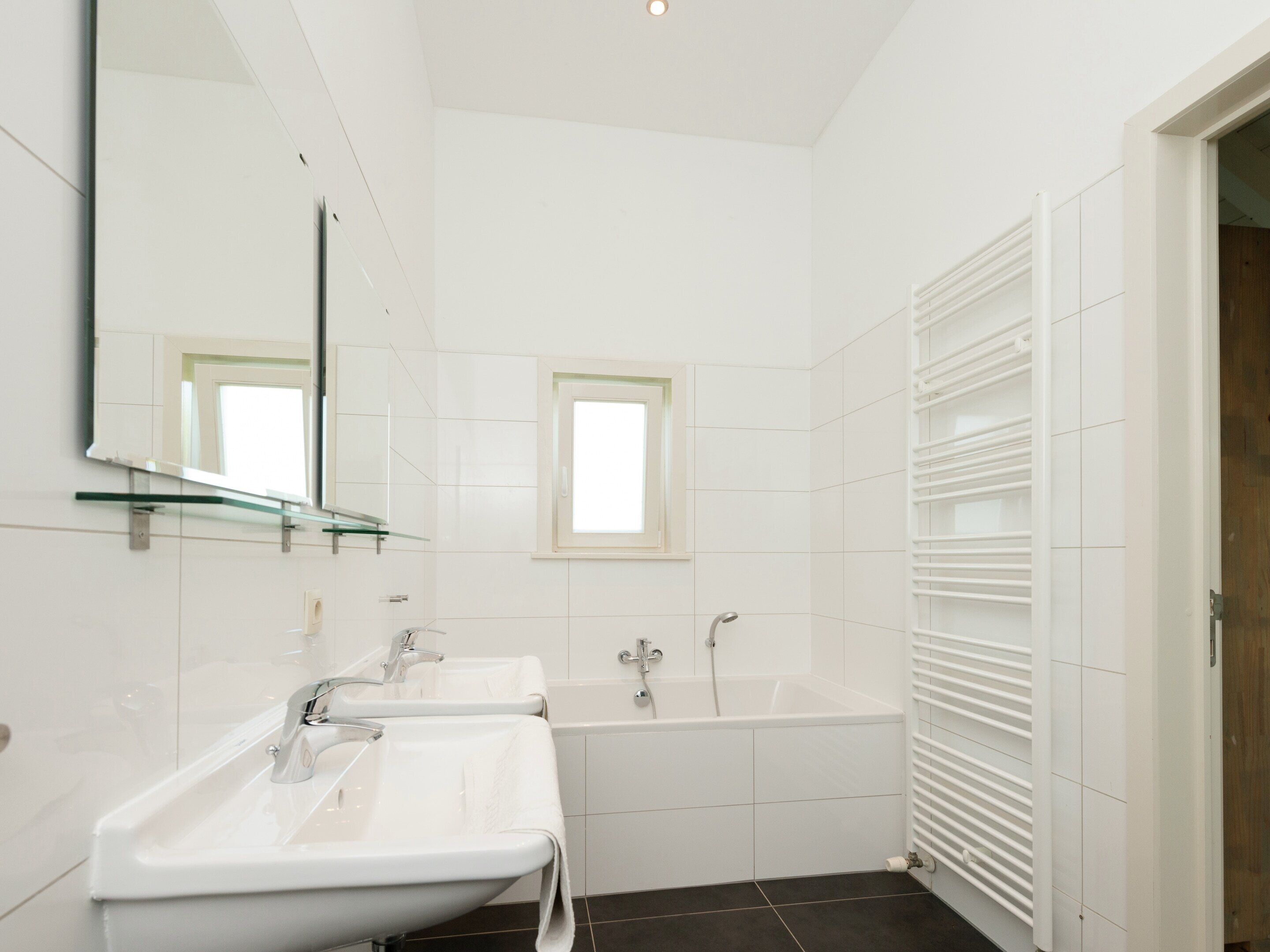 Une salle de bain moderne avec deux lavabos, une baignoire et une étagère en verre au-dessus des lavabos.