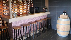 Un espace bar avec un présentoir à bouteilles de vin, des tabourets et un tonneau en bois.