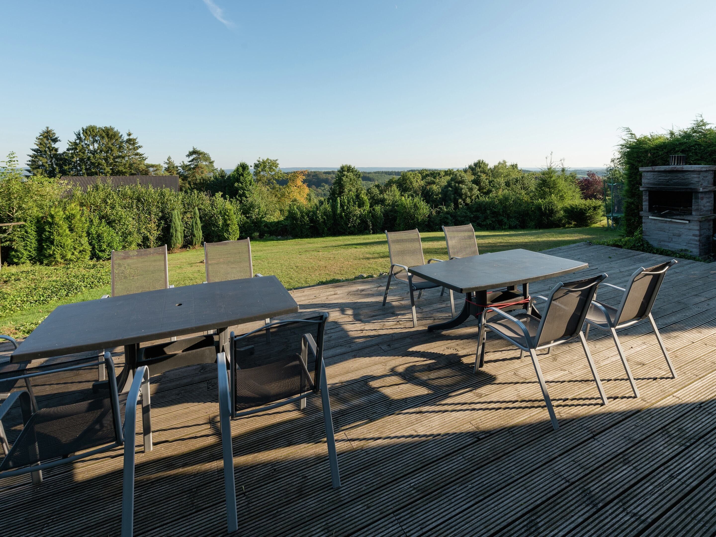 An outdoor deck with a table and chairs, surrounded by a garden and a stone fireplace.