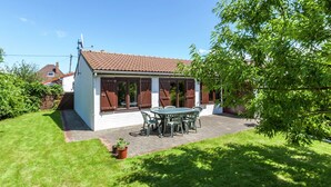 Ein Haus mit einem Ziegeldach, einer Terrasse mit Tisch und Stühlen sowie einem gepflegten Rasen.